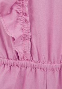 Rózsaszín anyag texturált felülettel, fodros szélekkel és rugalmas redőzéssel a derékon. A varrások a megfelelő színű cérnával láthatók.