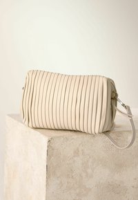 Borsa beige plissettata in materiale morbido, caratterizzata da una forma arrotondata e una tracolla staccabile. Superficie testurizzata con lieve lucentezza.