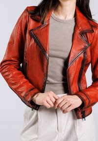 Rode leren motorjack met een gekartelde kraag, ritsmanchetten en zijzakken, gelaagd over een beige geribbelde top. Gladde textuur, getailleerd ontwerp.