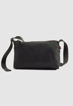 Mustade ristkülikukujuline õlakott, millel on reguleeritav kangast rihm ja ülemine lukuga sulgemine, heleda ühtse tausta ees.