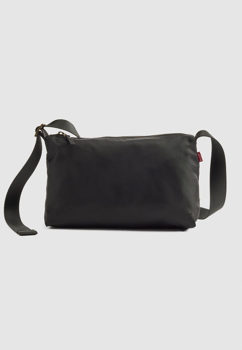 Bolso cruzado rectangular negro con correa de tela ajustable y cierre de cremallera en la parte superior, sobre un fondo claro y liso.
