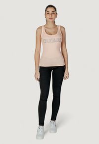 Canotta rosa chiaro con logo "GUESS", texture a coste, abbinata a jeans skinny neri e sneakers bianche. Design semplice e aderente.