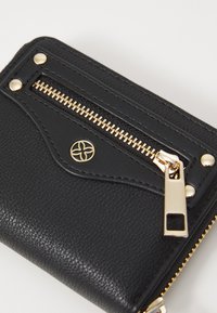 Cartera de cuero negro con cremallera dorada, superficie texturizada y herrajes decorativos. Presenta un bolsillo con cremallera y detalle de logo en relieve.