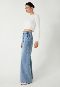 Witte cropped sweater en lichtblauwe wide-leg jeans, strakker rondom de taille met een rafelige zoom. Gladde textuur, minimale details, klassieke denimstijl.