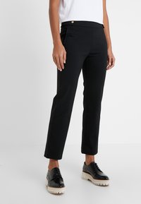 Czarne krótkie spodnie o gładkiej fakturze, z wąskim krojem, dwiema przednimi kieszeniami i złotym dekoracyjnym guzikiem. Połączone z czarnymi butami.