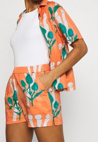 Kortärmad skjorta och shorts-set i orange tyg med gröna och vita blommönster; elastisk midja på shortsen; avslappnad passform.