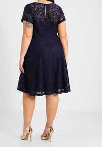 Navy blue lace dress with short sleeves, flared skirt, and a back zipper. Paired with shiny, metallic high heels.