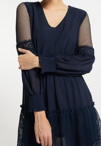 Robe bleu marine avec panneaux en maille transparente aux épaules, manches smockées, coupe ample avec ourlet en maille et détails volants.