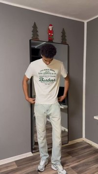 White graphic t-shirt with green text, light blue distressed jeans, and white sneakers. Mirrored wardrobe in a gray room.
