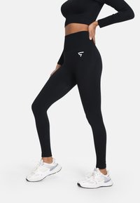 Čierne legíny s vysokým pásom a rebrovaným pásom, s bielym logom na zadnej strane. Hladká, elastická tkanina, priliehavý strih.
