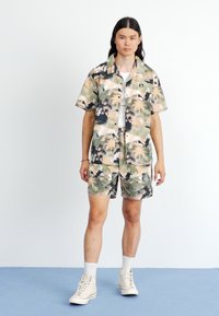 Korte mouwen, overhemd met knopen en bijpassende shorts in een palmbomenprint. Kleuren zijn groen, beige en zwart, met een losse pasvorm en stoftextuur.