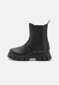 Botines negros con paneles laterales elásticos, que cuentan con una suela de goma gruesa y un acabado de cuero suave. Incluyen una lengüeta para facilitar su uso.