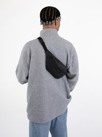Schwarze Umhängetasche, diagonal über einem grauen Fleece-Pullover getragen. Die Tasche hat eine glatte Textur und ist in Form streamlined.