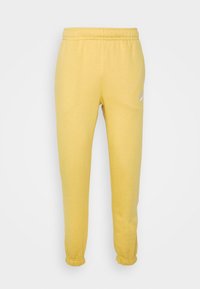 Gula sweatbyxor i bomull med resår i midjan, avsmalnande muddar vid anklarna och en liten logotyp tryckt på vänster lår.