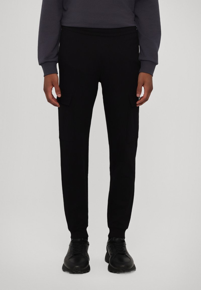 Svarte cargo-bukser i et mykt stoff, med to sidelommer, elastisk midje og tapered ben-design, kombinert med svarte sneakers.