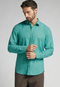 Turquoise overhemd met knopen en een subtiele textuur, lange mouwen en een klassieke kraag, gecombineerd met een paarse broek.