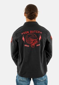 Camisa negra de manga larga con diseño gráfico rojo en la parte de atrás, que presenta el texto "Von Dutch", una pantera y acentos de relámpago. Corte casual.