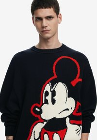 Strikket sweater i marineblå med et stort, farverigt Mickey Mouse grafisk motiv. Har rund hals, lange ærmer og ribbede manchetter. Glat tekstur.