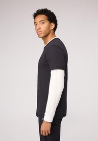 Zwart kortärm T-shirt bovenop een wit langärm shirt, met een ronde hals, gebogen zoom en een casual pasvorm.