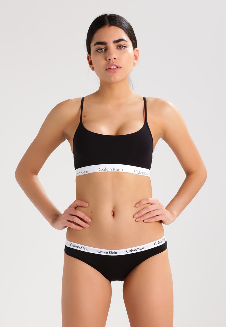 Svart Calvin Klein undertøysett med en bralette med tynne stropper og en matchende truse, begge med en hvit logo-stripe. Glatt tekstur.