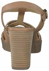 Tan platform sandal med et stroppet design, der har en bred, rippet hæl og et glat overmateriale. Spænde detaljer ved anklen.