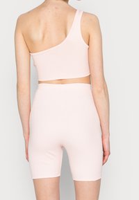 Světle růžový žebrovaný crop top s asymetrickým výstřihem, který je spárován s odpovídajícími vysokými bicyklovými šortkami s jemnou, hladkou texturou.