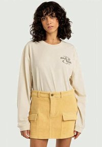 Cream long-sleeve shirt with graphic design paired with a yellow corduroy skirt featuring two front pockets and button closure.