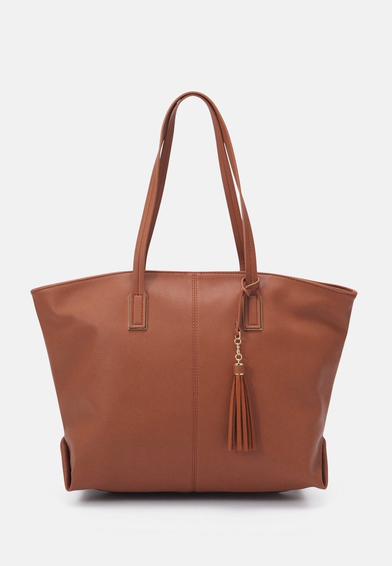 Sac cabas en cuir marron avec double bandoulière et un pompon décoratif suspendu à une bandoulière.