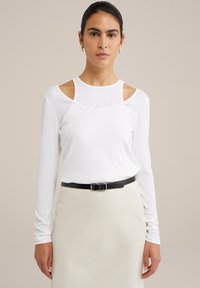 Balta ilga rankovė viršutinė dalis su pečių išpjovomis, pagaminta iš lengvo audinio. Derinama su juodu diržu, uždėtu ant šviesios sijono.