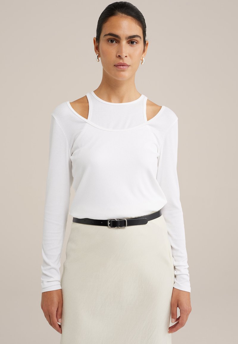 Balta ilga rankovė viršutinė dalis su pečių išpjovomis, pagaminta iš lengvo audinio. Derinama su juodu diržu, uždėtu ant šviesios sijono.