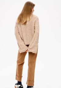 Beige gestrickter Pullover mit lockerer Passform und gerippter Textur, kombiniert mit braunen Cordhosen und schwarzen Sneakers mit weißen Akzenten.