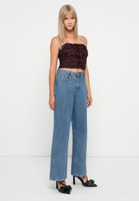 Dark burgundy cropped strapless top with textured floral design, paired with high-waisted light blue wide-leg jeans and black heeled shoes.