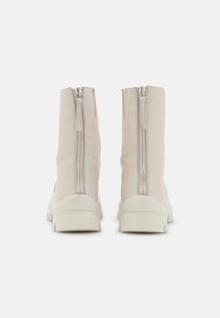 Botines beige con doble cremallera en la parte trasera, parte superior de cuero texturizado y suela blanca gruesa. Acabado suave con un diseño minimalista.