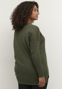 Maglione a maglia verde oliva con vestibilità rilassata, polsini a costine e spacchi laterali. Tessuto leggero, maniche lunghe e scollatura rotonda.