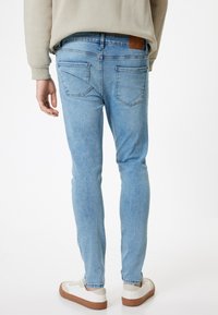 Jeans in denim azzurro chiaro con una vestibilità slim, dotati di tasche posteriori, leggere sfumature e una toppa in pelle marrone sulla vita.