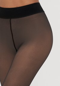 Meias pretas, transparentes, com uma textura suave e uma cintura larga e elástica. Apresentam uma costura subtil ao longo do centro para um visual ajustado.