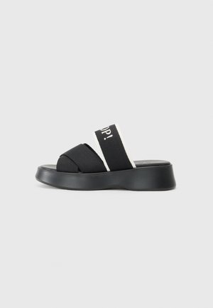 Zwarte slip-on sandaal met dikke elastische banden met witte accenten. Verhoogde platformzool met een gladde textuur. Geen zichtbare hardwaredetails.