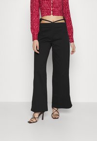 Calças largas pretas com uma textura suave e cintura alta. Combinadas com um top cropped ajustado de padrão vermelho e sandálias de salto com tiras.