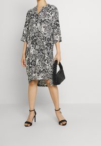 Robe à imprimé léopard en tissu léger, avec un décolleté en V, des manches trois-quarts et un ourlet asymétrique. Associée à un sac à main noir tressé.