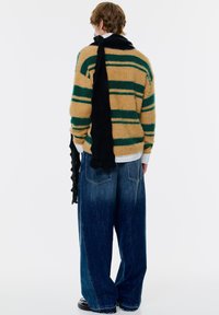 Nadměrný žlutý a zelený pruhovaný svetr s černým šátkem, př paired s širokými modrými džínami s texturovaným povrchem.