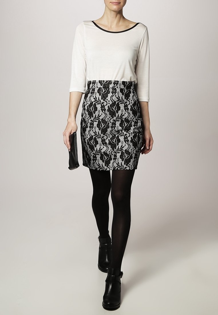 Svart och vit mönstrad kjol med spetsdesign, tillsammans med en åtsittande krämfärgad topp och svarta strumpbyxor. Inkluderar en svart kuvertväska och ankelstövlar.