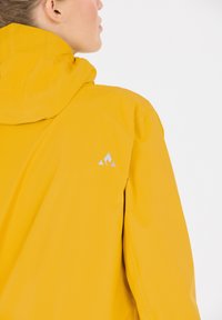 Lyst gul vandtæt jakke med hætte, udstyret med et diskret logo i sølv på ryggen og en glat, mat finish.