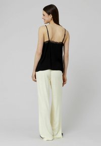 Camisole noire à bordures en dentelle avec des bretelles fines, associée à un pantalon large crème en tissu léger et texturé.