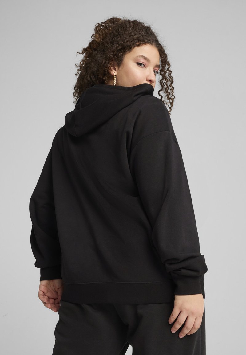 Haut à capuche noir en tissu doux, avec une coupe décontractée. L'ourlet et les poignets sont côtelés, et il possède une grande poche à l'avant.