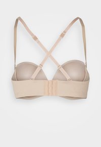 Beige beha, gladde cups, verstelbare banden die een X op de rug vormen, haak-en-oogsluiting, met een zachte textuur en naadloos ontwerp.