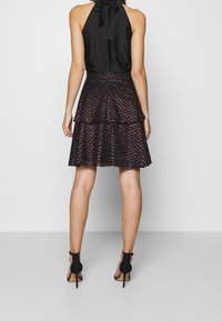 Svart halterneck-top med en slinga vid halsen, tillsammans med en lager-på-lager svart kjol med ett zigzag-mönster i rosa. Svarta högklackade sandaler.