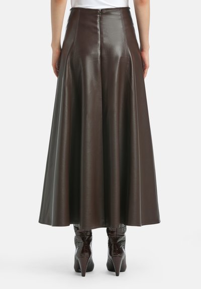 Gonna maxi in finta pelle marrone con silhouette svasata, cuciture visibili e cerniera sul retro, abbinata a stivaletti texani con tacco alto e texture.