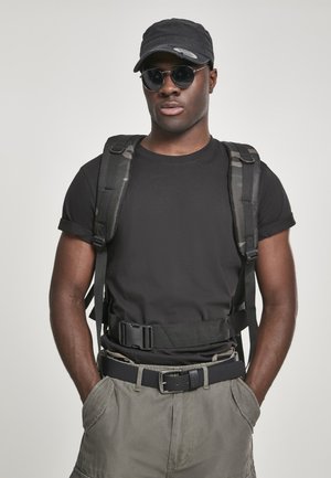 Black t-shirt and gray cargo shorts worn with a tactical backpack and wide black belt. Accessories include a black cap and sunglasses.