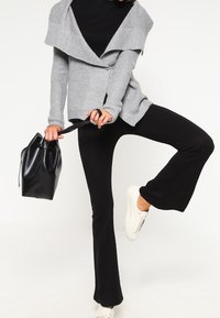 Šedý pletený cardigan s oversized límcem, kombinovaný s černými kalhotami s rozšířenými nohavicemi a bílými teniskami. Černá kabelka držena v jedné ruce.