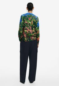 Maglione a maglia multicolore con un design floreale in verde, rosa e blu, abbinato a pantaloni neri a gamba larga con orlo a coste.